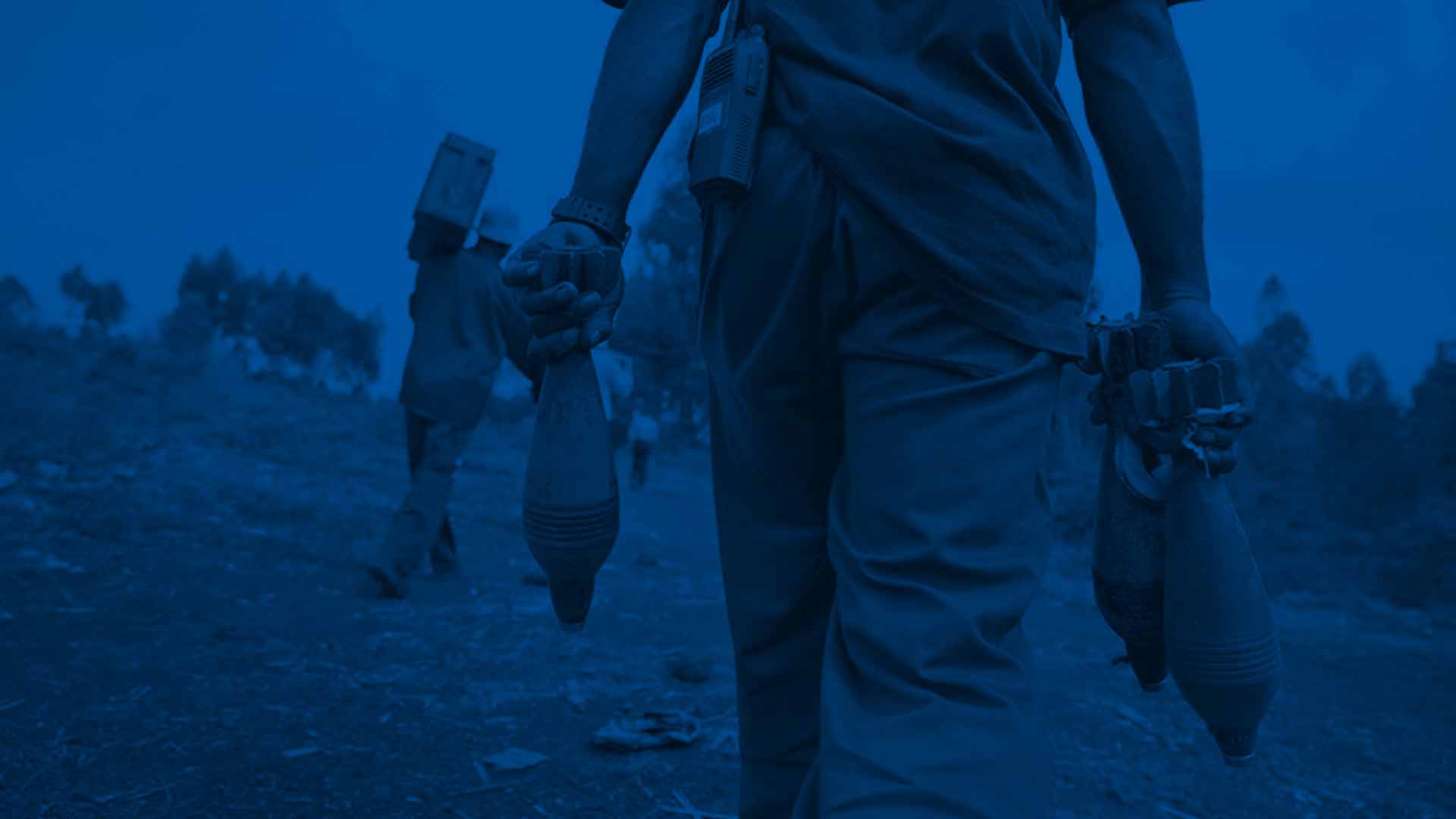 A man carries rocket-propelled grenades with his back turned to the camera